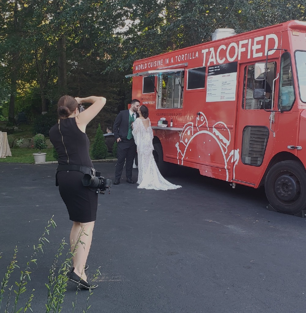 Photographer aiming camera at bride and groom in front of red food truck